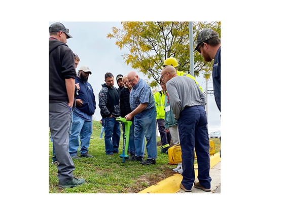 A locator instructor training a group of students outside next to a curb and a tree